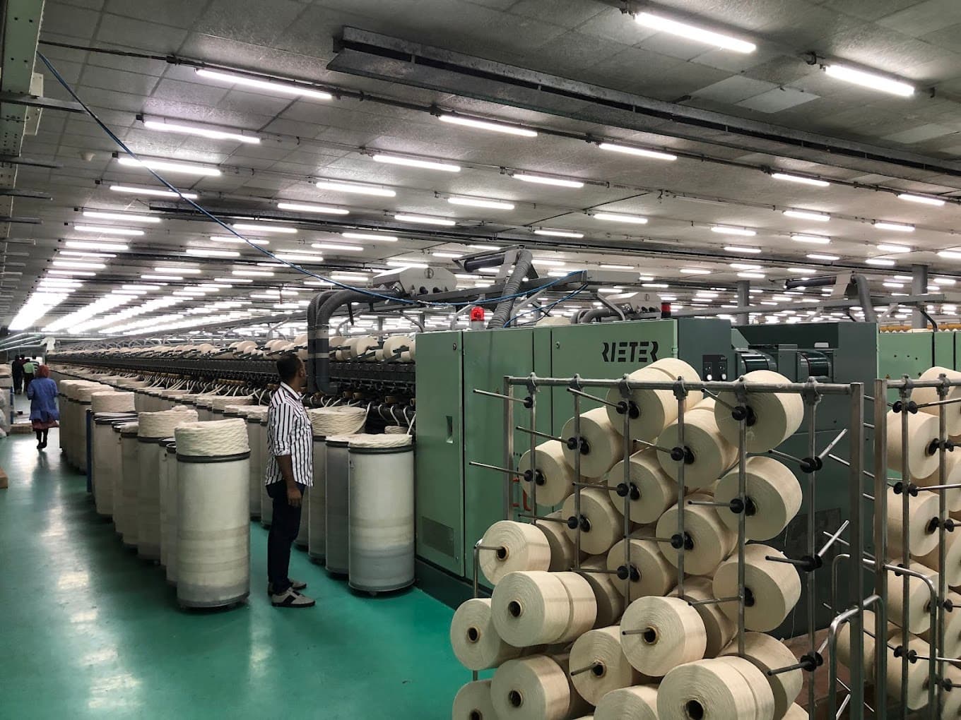 Argon Denims spinning floor · Rieter ring frames, white yarn cones, operator in striped shirt.